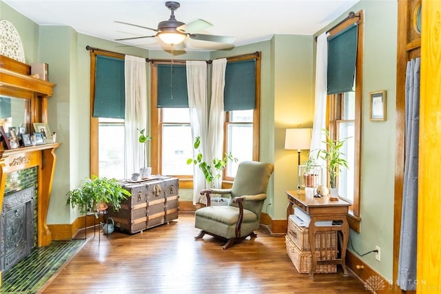 living area featuring ceiling fan, a premium fireplace, baseboards, and hardwood / wood-style flooring