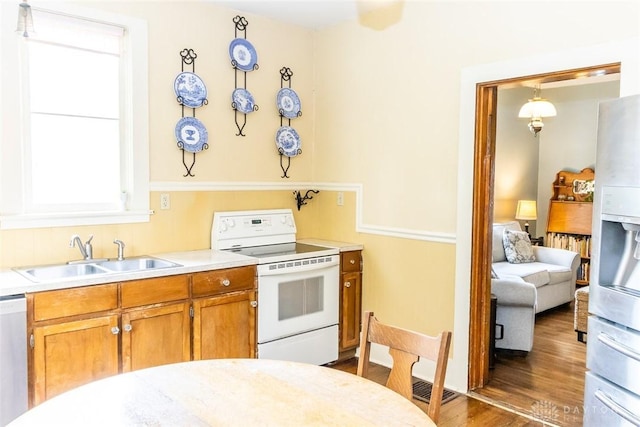 kitchen featuring white appliances, wood finished floors, a sink, light countertops, and brown cabinets