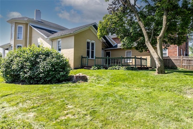 back of house with brick siding, a yard, a chimney, fence, and a deck