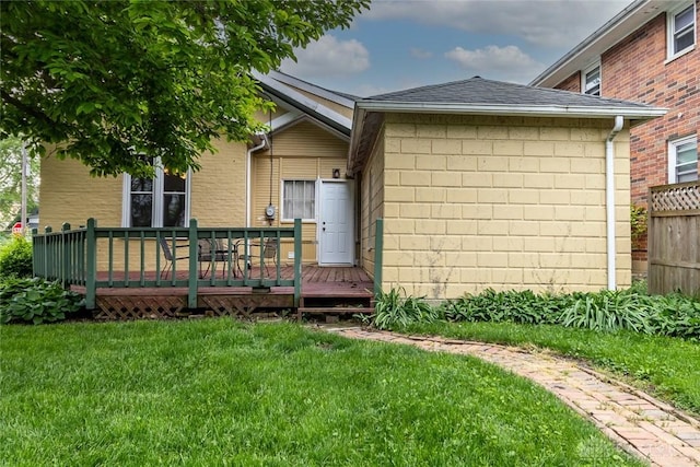 back of property featuring roof with shingles, a yard, brick siding, fence, and a wooden deck