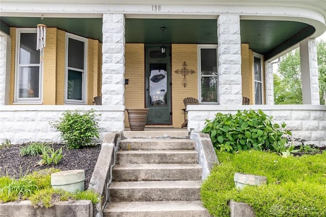 view of exterior entry with stone siding and a porch