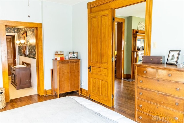 bedroom with connected bathroom, a sink, baseboards, and wood finished floors