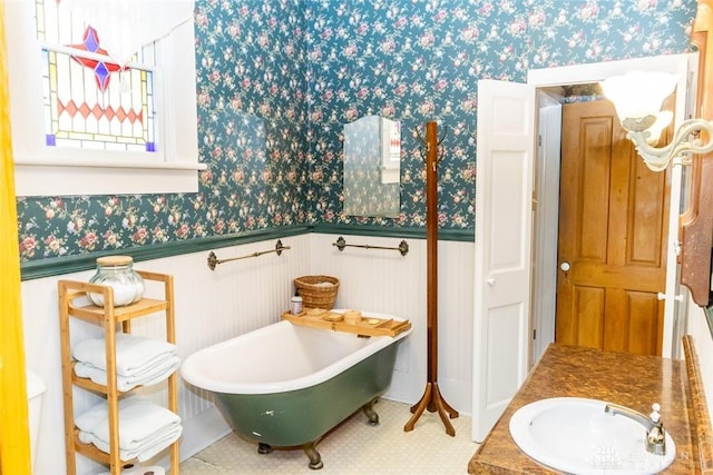 full bathroom featuring a freestanding tub, wainscoting, a sink, and wallpapered walls