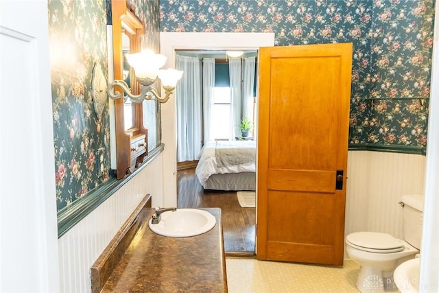 interior space featuring toilet, wainscoting, a sink, ensuite bath, and wallpapered walls