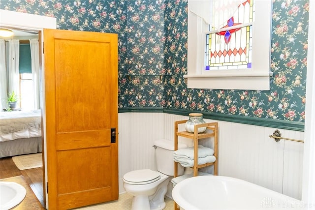 ensuite bathroom featuring wallpapered walls, a wealth of natural light, and a wainscoted wall