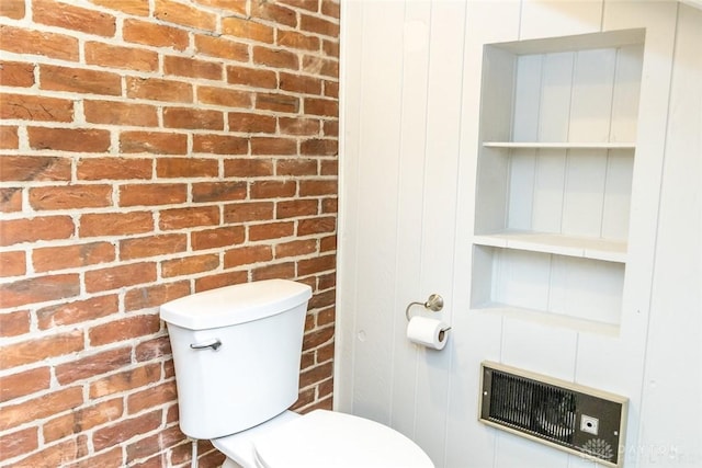 bathroom with brick wall, visible vents, and toilet