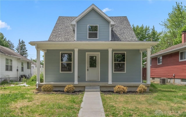 bungalow featuring a porch, a front yard, roof with shingles, and central AC