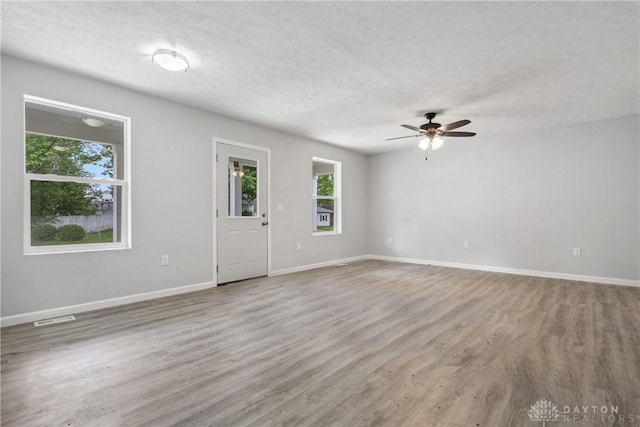 empty room with light wood-type flooring, visible vents, a textured ceiling, and baseboards