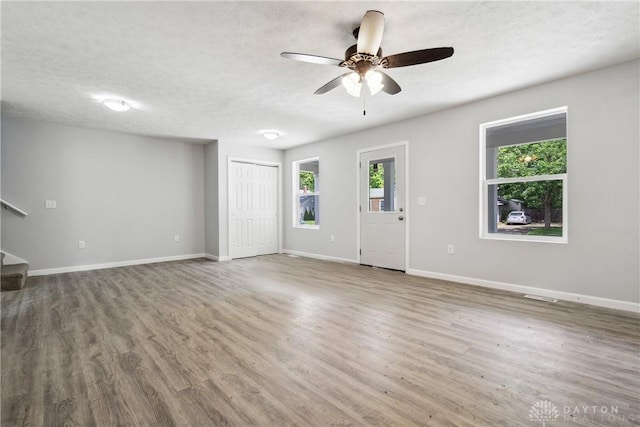 unfurnished living room featuring stairs, baseboards, a textured ceiling, and wood finished floors