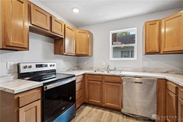 kitchen featuring light wood-style floors, appliances with stainless steel finishes, brown cabinets, and a sink