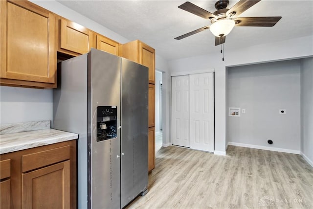 kitchen with ceiling fan, baseboards, light stone countertops, light wood finished floors, and stainless steel fridge