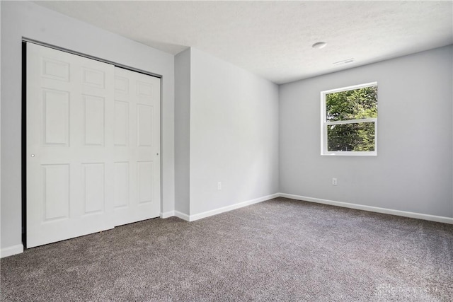 unfurnished bedroom featuring a textured ceiling, carpet flooring, visible vents, baseboards, and a closet