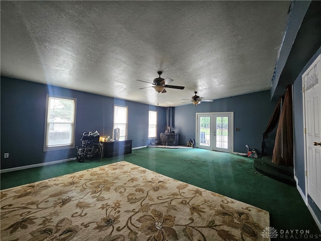 carpeted empty room featuring a wood stove, a textured ceiling, ceiling fan, and french doors