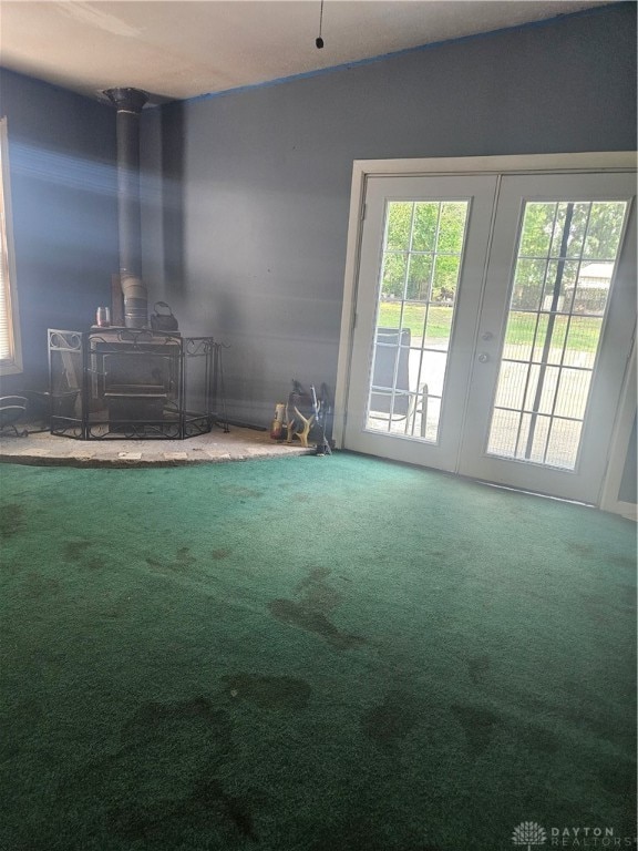 unfurnished room featuring a wood stove, a healthy amount of sunlight, carpet, and french doors