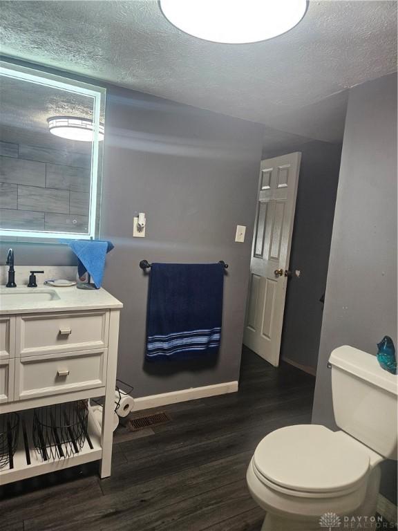 bathroom with vanity, wood finished floors, baseboards, a textured ceiling, and toilet