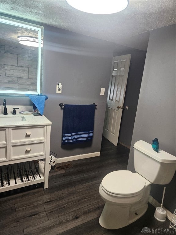 bathroom with a textured ceiling, vanity, wood-type flooring, and toilet