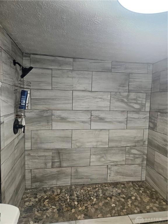 full bathroom featuring a tile shower, a textured ceiling, and toilet