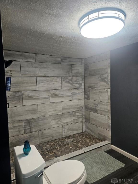 bathroom with wood finished floors, baseboards, toilet, a textured ceiling, and a shower stall