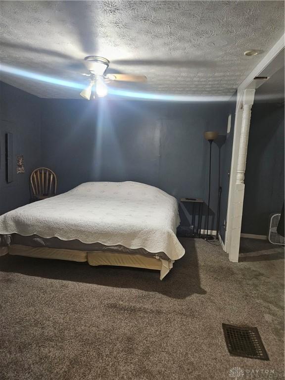 bedroom featuring a textured ceiling, dark colored carpet, and a ceiling fan