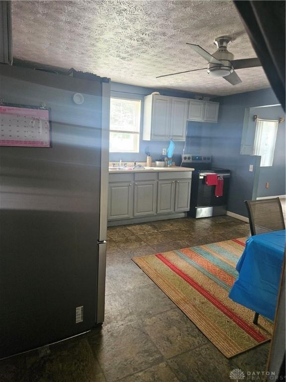 kitchen featuring stainless steel fridge, dark tile patterned flooring, a textured ceiling, electric range, and ceiling fan