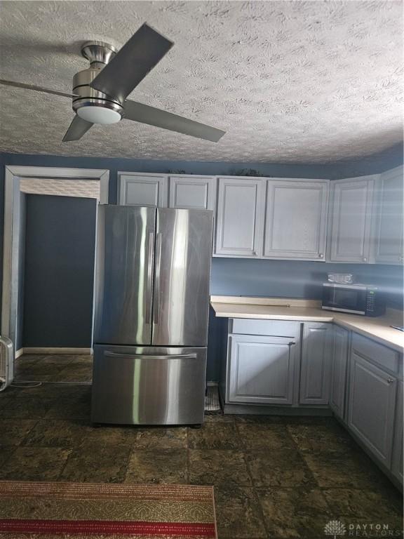 kitchen with stainless steel fridge, a textured ceiling, ceiling fan, and dark tile patterned flooring