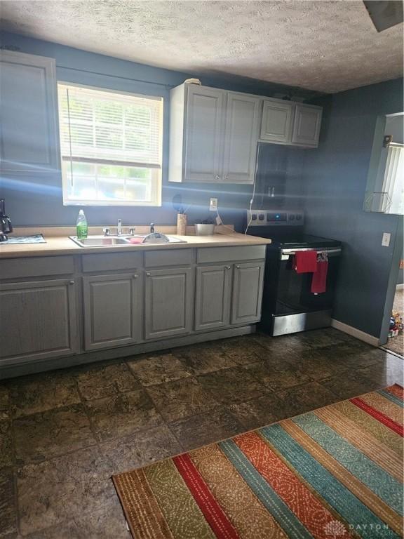 kitchen with gray cabinets, stainless steel electric range oven, a textured ceiling, and dark tile patterned flooring