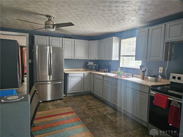 kitchen featuring ceiling fan, sink, appliances with stainless steel finishes, a textured ceiling, and dark tile patterned flooring