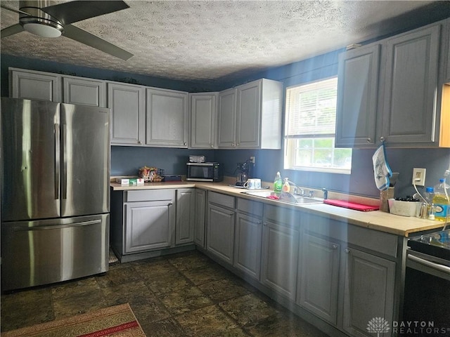 kitchen featuring freestanding refrigerator, light countertops, a sink, black microwave, and gray cabinets