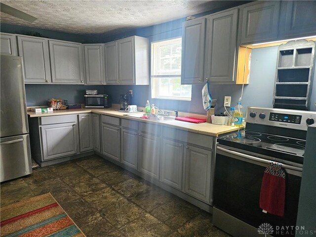 kitchen featuring gray cabinetry, dark tile patterned floors, a textured ceiling, and stainless steel appliances