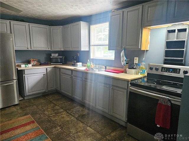 kitchen featuring light countertops, stainless steel appliances, a sink, a textured ceiling, and stone finish flooring