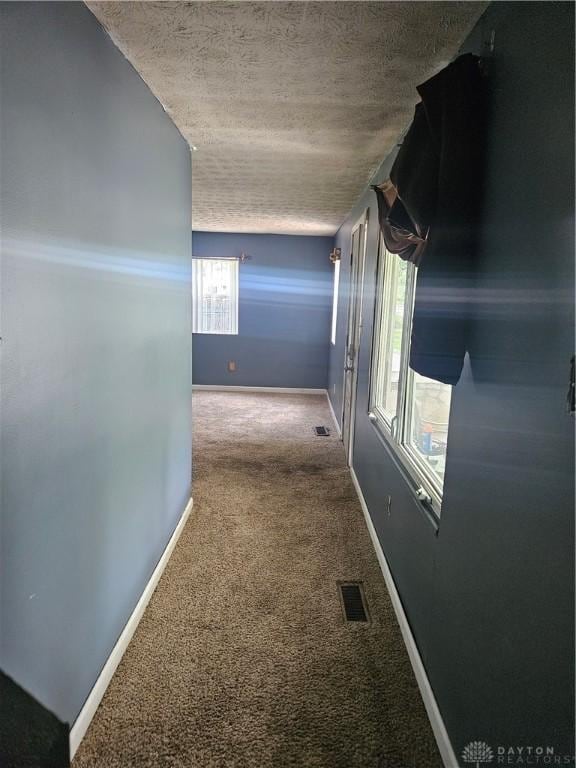 hallway with baseboards, visible vents, carpet, and a textured ceiling