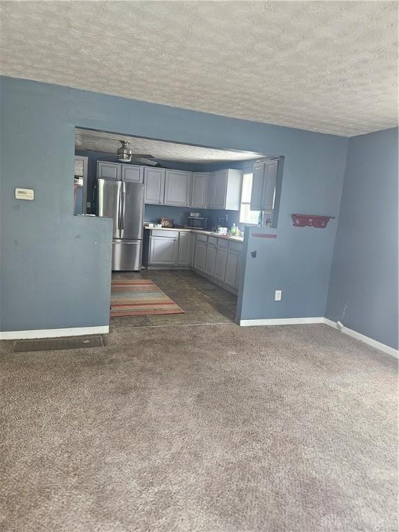 kitchen featuring freestanding refrigerator, baseboards, dark carpet, a textured ceiling, and gray cabinetry