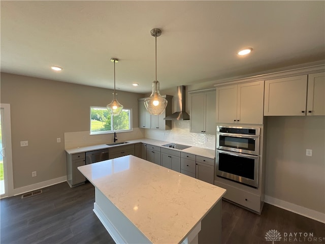 kitchen with wall chimney range hood, dark hardwood / wood-style floors, hanging light fixtures, stainless steel appliances, and sink