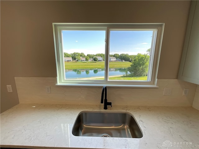 interior details featuring light stone countertops, sink, a water view, and backsplash