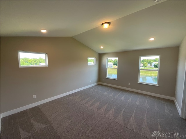 spare room featuring vaulted ceiling and dark colored carpet