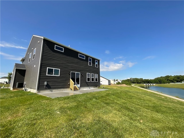 rear view of house with a water view, a patio area, central AC, and a lawn