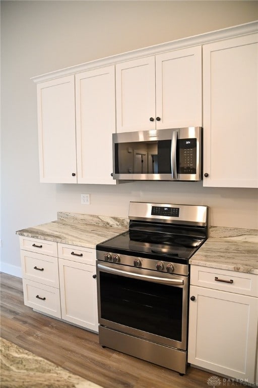 kitchen with appliances with stainless steel finishes, white cabinets, light stone countertops, and hardwood / wood-style floors