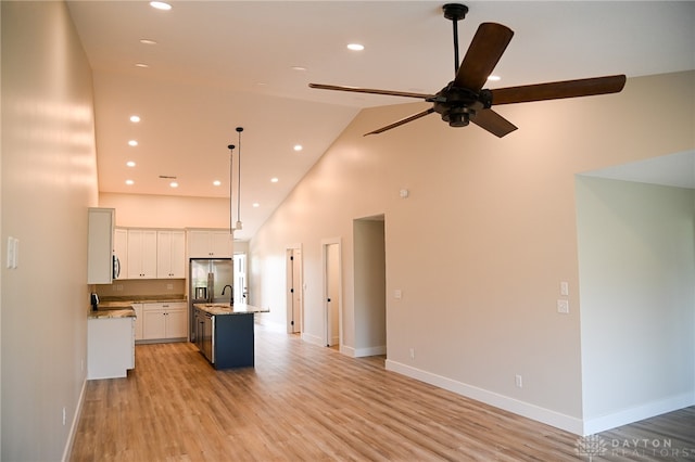 kitchen with white cabinets, a center island with sink, high vaulted ceiling, light wood-type flooring, and pendant lighting