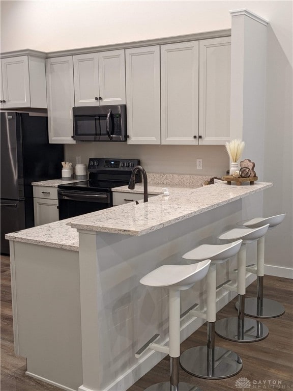 kitchen featuring a kitchen bar, light stone counters, dark hardwood / wood-style flooring, and electric range oven