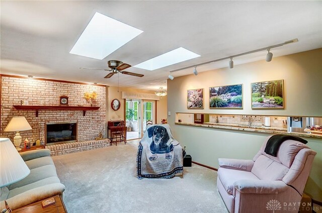 carpeted living room with ceiling fan, a brick fireplace, track lighting, and a skylight