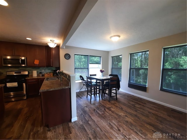 kitchen with appliances with stainless steel finishes, a textured ceiling, dark stone counters, dark hardwood / wood-style floors, and sink