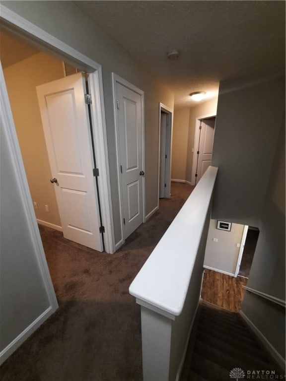 hallway with dark carpet and a textured ceiling