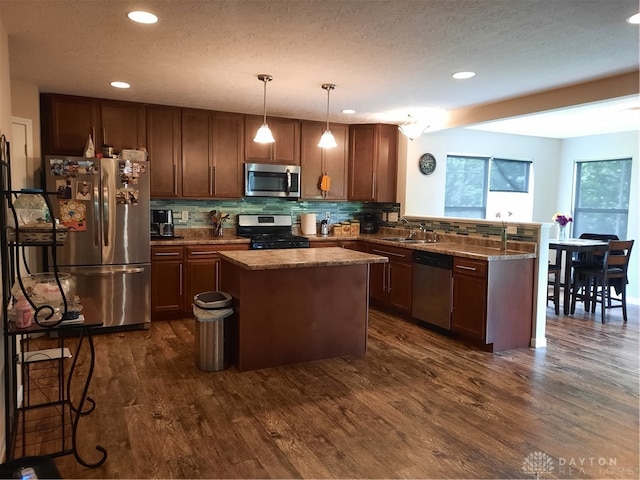 kitchen with sink, a kitchen island, decorative light fixtures, appliances with stainless steel finishes, and dark hardwood / wood-style floors