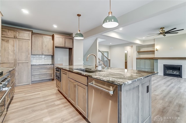 kitchen with a center island with sink, stainless steel dishwasher, hanging light fixtures, and light hardwood / wood-style flooring