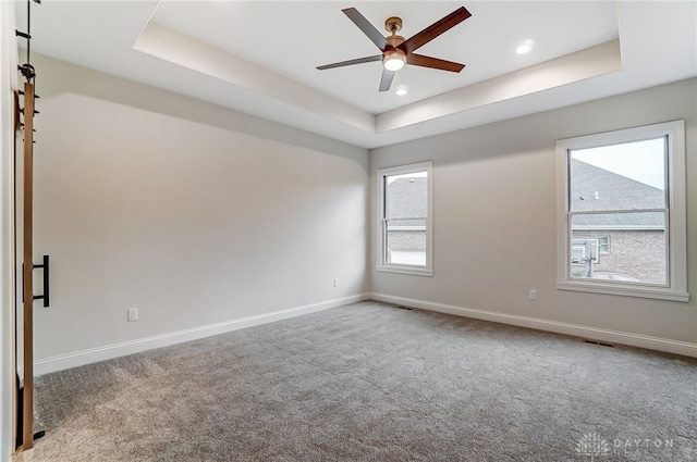 carpeted empty room with a raised ceiling and ceiling fan