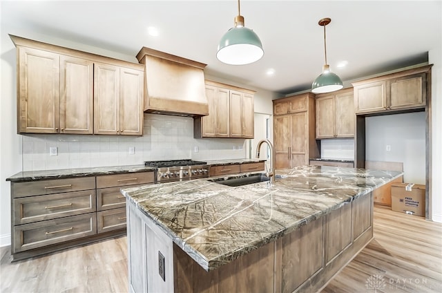 kitchen featuring pendant lighting, premium range hood, a large island with sink, sink, and light hardwood / wood-style floors