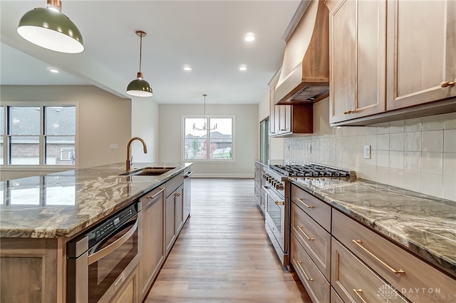 kitchen with premium range hood, sink, high end stainless steel range oven, hanging light fixtures, and light wood-type flooring