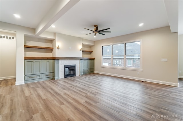 unfurnished living room with beamed ceiling, ceiling fan, a tiled fireplace, and light hardwood / wood-style flooring