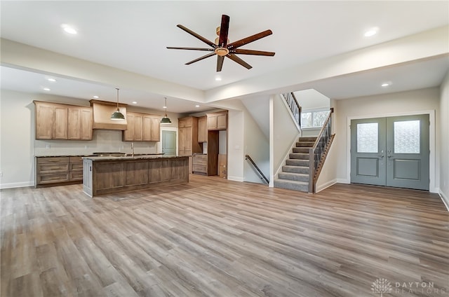 kitchen featuring custom range hood, light hardwood / wood-style flooring, hanging light fixtures, and an island with sink