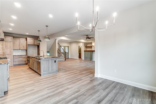 kitchen featuring ceiling fan, light stone counters, an island with sink, light hardwood / wood-style floors, and decorative light fixtures